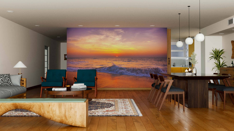 A modern living-dining room features wooden floors, mid-century furniture, and a large Sunset on Tropical Beach Wall Mural depicting colorful waves and clouds, adding warmth and a scenic focal point to the space.