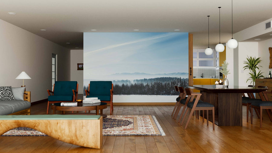Modern open living-dining area with wood floors, mid-century furniture, and hanging lights. A large Sunshine and Winter Snowy Mountain Wall Mural is a focal point. Area rugs, wooden table, and teal chairs enhance the cozy, stylish space.