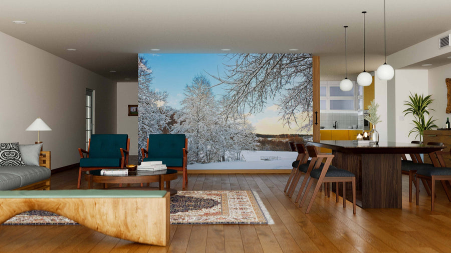 A modern open-plan living and dining room with wooden floors, teal armchairs, and a large dining table is filled with natural light from a wall-sized window and the Trees with Snow in Winter Wall Mural depicting snowy trees and blue sky.