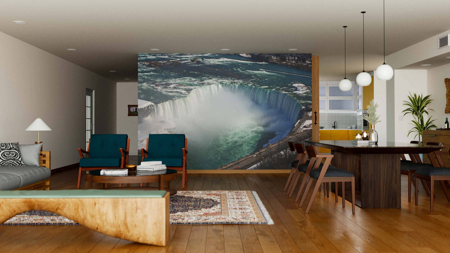 A modern living and dining room with wooden floors and furniture features the View at Niagara Falls Wall Mural as a dramatic focal point. Mid-century chairs, a dining table, and a cozy sofa complete this stylish, open-concept space.