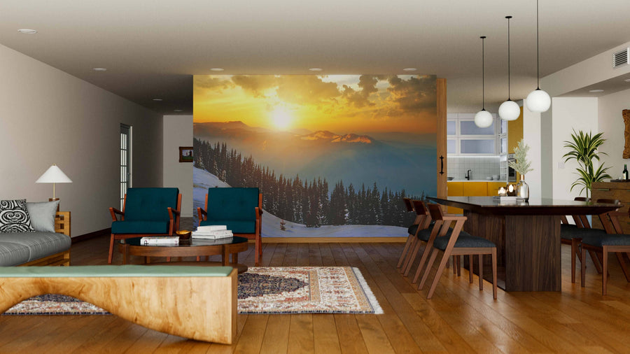 A modern open-plan living and dining room features wooden floors, teal armchairs, a large dining table, and the "Winter Landscape with High Peaks Wall Mural," casting warm light that enhances the cozy and inviting atmosphere.