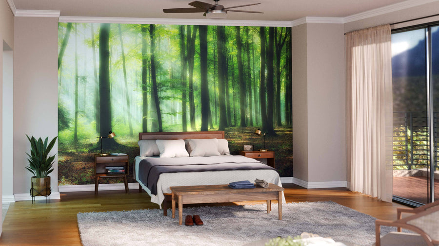 A cozy bedroom features a wooden bed, white bedding, two nightstands with lamps, a bench, and the Morning in the Forest Wall Mural. A potted plant, gray rug, and glass doors with beige curtains complete the modern décor.