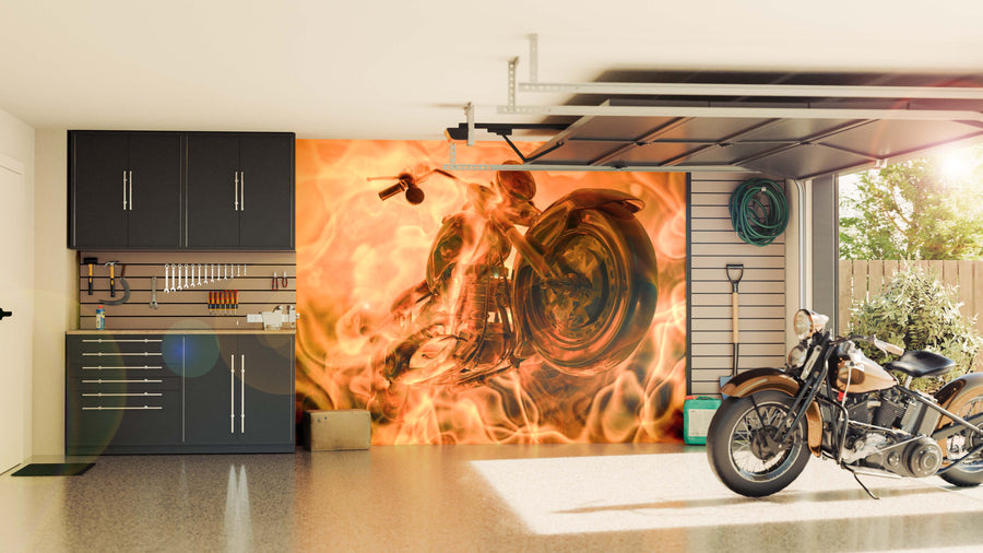 A modern garage with black cabinets, organized tools, and a motorcycle. The back wall displays the Bike in Flames Wall Mural, while sunlight pours in through the open door, lighting up the space and revealing a tree outside.