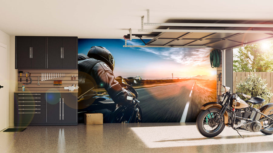 A tidy garage with dark cabinets, tools hung neatly, and a classic motorcycle parked. The back wall displays the Endless Open Road Wall Mural, showing a motorcyclist at sunset and adding depth. The garage door is partially open.