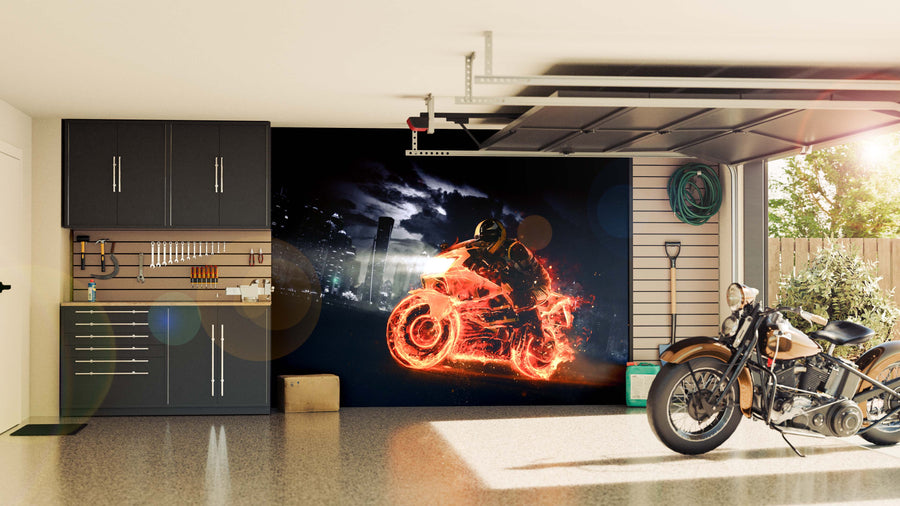 A modern garage with black cabinets, wall-mounted tools, and a vintage motorcycle features the Fiery Ride Wall Mural—a dramatic mural of a flaming motorcycle at night—creating a bold, striking focal point on the back wall.