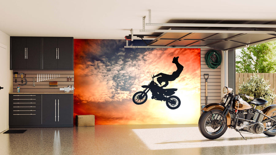 A modern garage features sleek black cabinets, organized tools, and a Freestyle Motocross Wall Mural showing a rider mid-air at sunset. A classic motorcycle rests on the shiny floor near the open garage door.