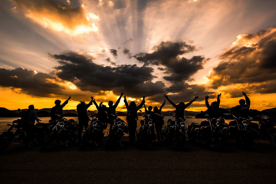 A modern garage with black cabinets, a tool rack, and a motorcycle. The back wall showcases the Motorcycle Group Wall Mural featuring cheering people at sunset. Sunlight fills the clean, organized space.