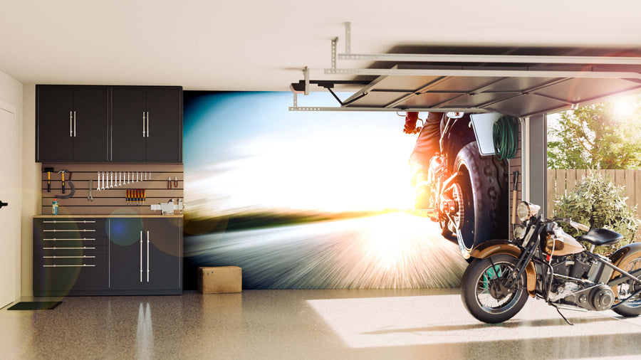 A clean, modern garage with black cabinets, organized tools, and a retro motorcycle. The back wall features the Motorbike on Road Wall Mural, showing a close-up of a speeding motorcycle with sunlight and motion blur for dynamic impact.