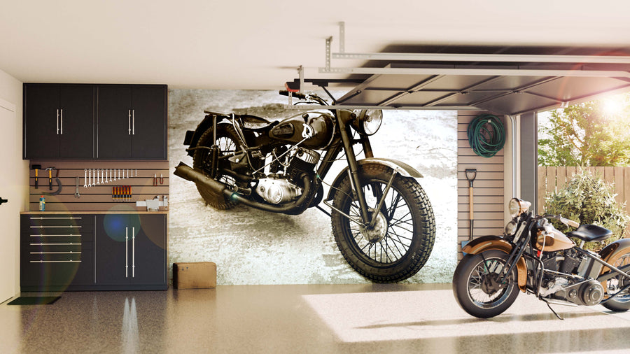 A modern garage with sleek black cabinets, organized tools, and an Old Motorcycle Wall Mural. Sunlight highlights a classic bike and a green hose by the window that overlooks trees.