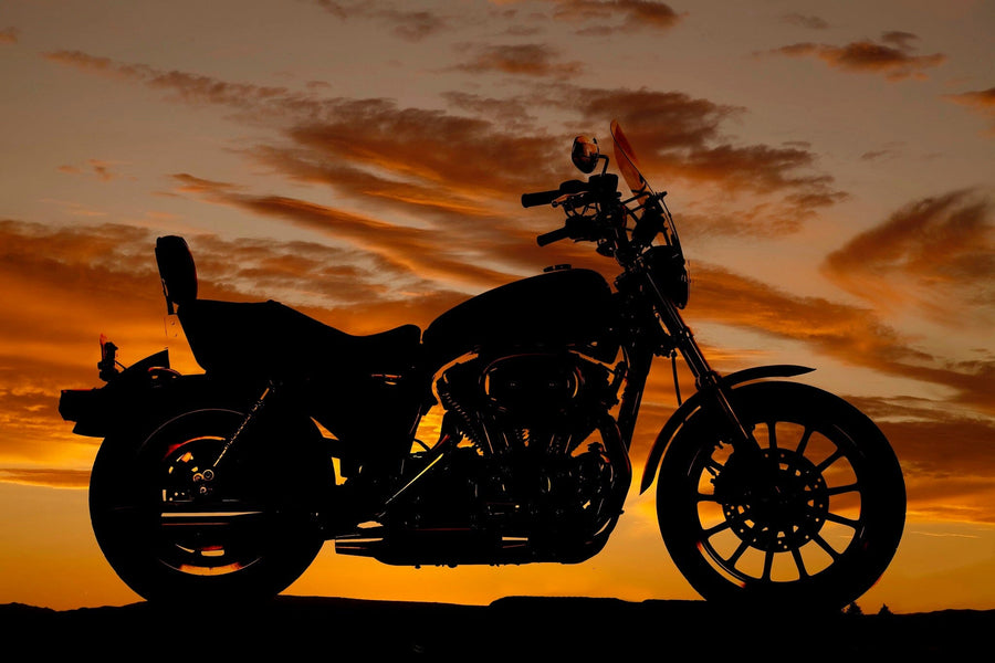 A modern garage showcases sleek black cabinets, a motorcycle on a shiny floor, and the Motorcycle Silhouette Wall Mural—a vibrant display of a bike against an orange sunset—while sunlight streams in from the open door.