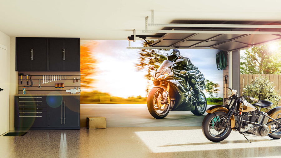 A modern garage with sleek black cabinets and a classic motorcycle features the Sunset Speed Ride Wall Mural on the back wall, displaying a vibrant sport bike scene as sunlight streams in, completing the polished look.