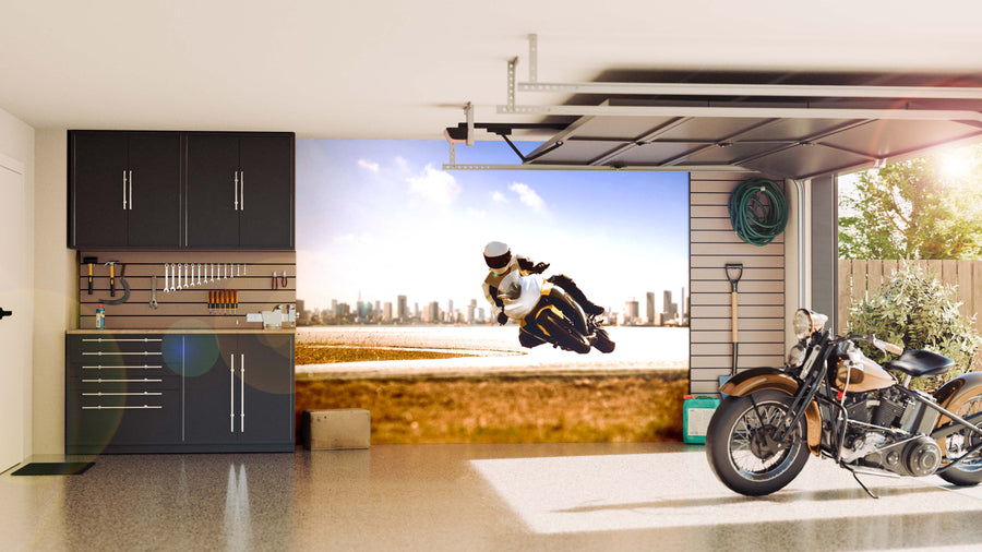 A modern garage with black cabinets, hanging tools, and a classic motorcycle is opened to reveal the Urban Speed Chase Wall Mural—a dynamic cityscape showing a motorcyclist leaning into a turn under a bright sky.