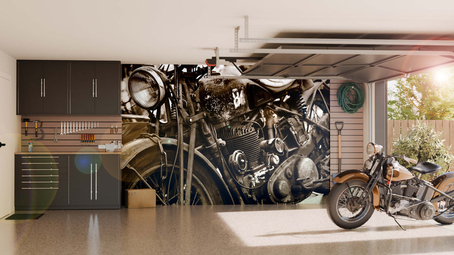 A clean garage with cabinets, organized tools, and a vintage motorcycle. Sunlight streams in as the back wall features the Vintage Ride Wall Mural—a peel and stick close-up black-and-white classic motorcycle engine design.