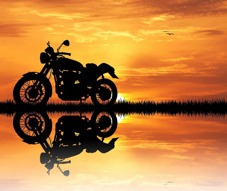 A modern garage with black cabinets, organized tools, and a classic motorcycle features the Motorcycle at Sunset Wall Mural—a peel and stick mural depicting a motorcycle’s silhouette on water framed by a vivid orange sunset.