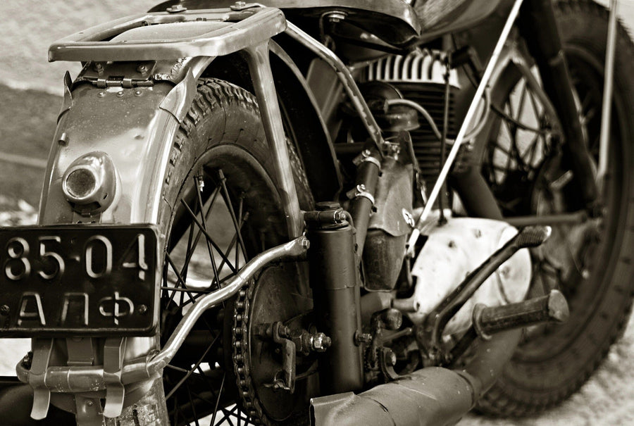 A modern garage with sleek black cabinets and organized tools features the Old Motorcycle Engine Wall Mural in sepia tones on the back wall, highlighted by sunlight streaming through the open door and a vintage motorcycle parked inside.