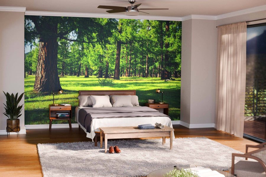 A modern living-dining room with wood floors and mid-century furniture features a Pine Forest with Green Grass Wall Mural. Pendant lights hang over a dark wood dining table; green armchairs and sofa complete the seating area, with a kitchen in the background.