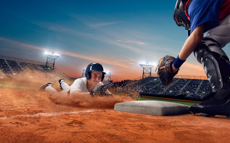 A bedroom features the Players Infield Wall Mural—a peel and stick design of a baseball player sliding home as a catcher tags him. Paired with a daybed, desk, chair, white cabinets, and sunlit wooden floors, it adds vibrant energy to the space.