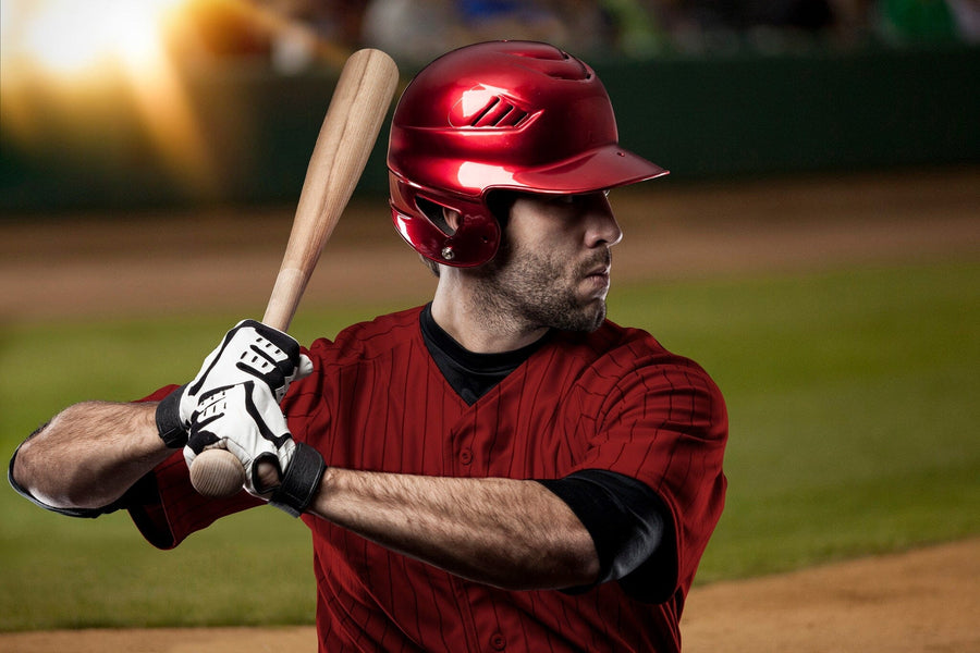 A bedroom with a bed, desk, and computer features the Power Stance Wall Mural of a baseball player in a red uniform mid-swing. Sunlight streams through the window, and a soccer ball rests near the bed on the wooden floor.