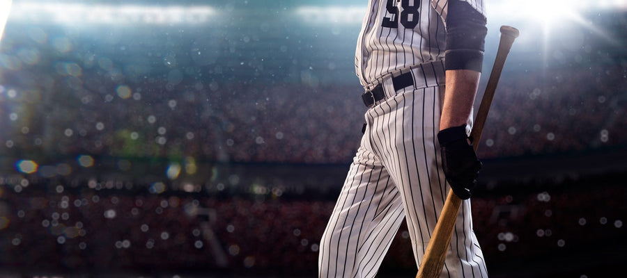 A modern bedroom with a desk, chair, and daybed features the Baseball Player Walking Wall Mural showing a pinstriped player with bat from the chest down. Natural light filters in through blinds, and a soccer ball sits on the floor.