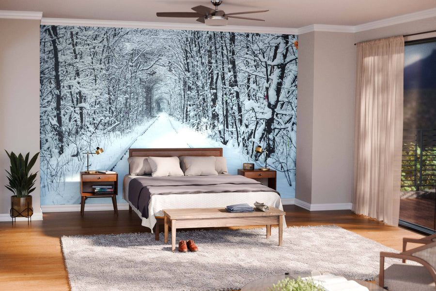 Modern living and dining room with wooden floors and furniture, featuring the 'Railway in the Winter Wall Mural,' a peel and stick mural depicting a snowy forest path lined with leafless trees that adds depth against the warm interior tones.