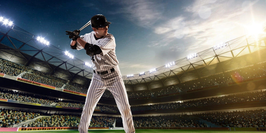 A bedroom with a bed, chair, desk, white wardrobe, window blinds, and sports decor features the Ready to Bat Wall Mural―a large peel and stick mural of a baseball player in uniform preparing to bat in a stadium.