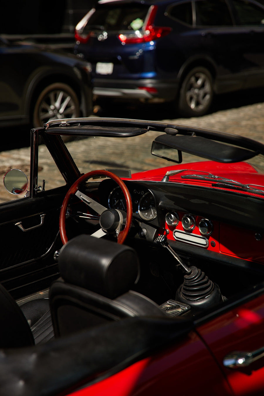 A modern bedroom with a white wardrobe, computer desk, black gaming chair, and a bed with blue and yellow pillows. The Red Vintage Car Wall Mural adds flair as sunlight streams in, highlighting the wooden floor and soccer ball.