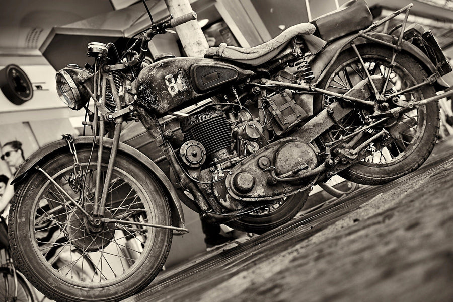 A modern garage with sleek black cabinets and tool storage showcases the Rustic Charm Wall Mural—a striking black-and-white vintage motorcycle design. Another vintage bike sits on the floor, sunlight pours in, and greenery is visible outside.