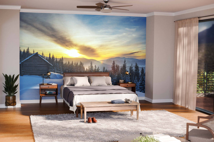 A modern living-dining area with wooden floors, teal armchairs, and globe pendants features the "Winter on a Mountain Range Wall Mural," showcasing a snowy landscape with a golden sunset to warm and enliven this cozy, open-concept space.