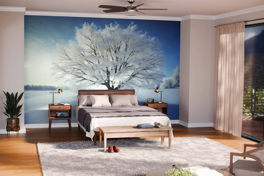A modern living-dining room with wood floors, blue armchairs, and a gray sofa features the Snow-Covered Tree Wall Mural as a focal point on the far wall, while warm natural light and hanging lamps enhance the contemporary feel.