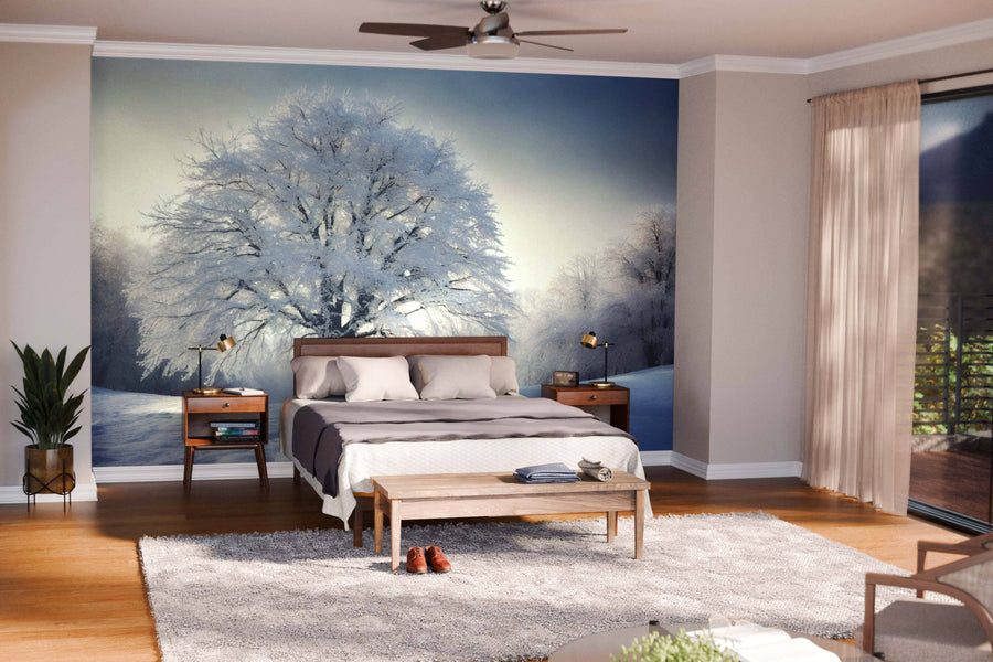 A cozy, modern living-dining room with wooden floors and pendant lights features the Snow-Covered Tree at Sunset Wall Mural, adding a serene, natural touch to the stylish space with its wintry landscape of bare trees.