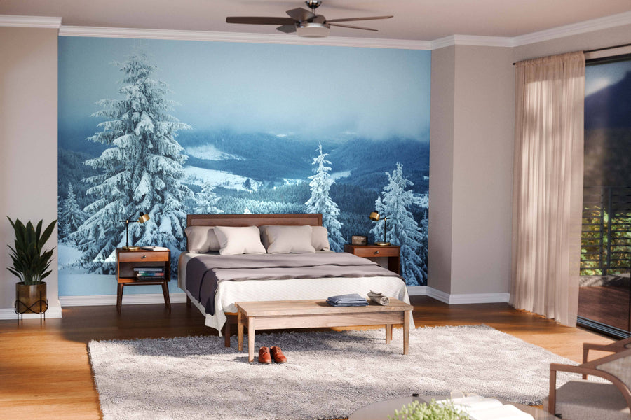 A modern living and dining area with wood floors, teal and brown furniture, and pendant lights is warmed by the Snowy Hill with Fir Trees Wall Mural, adding a wintry outdoor feel to the cozy, stylish interior.
