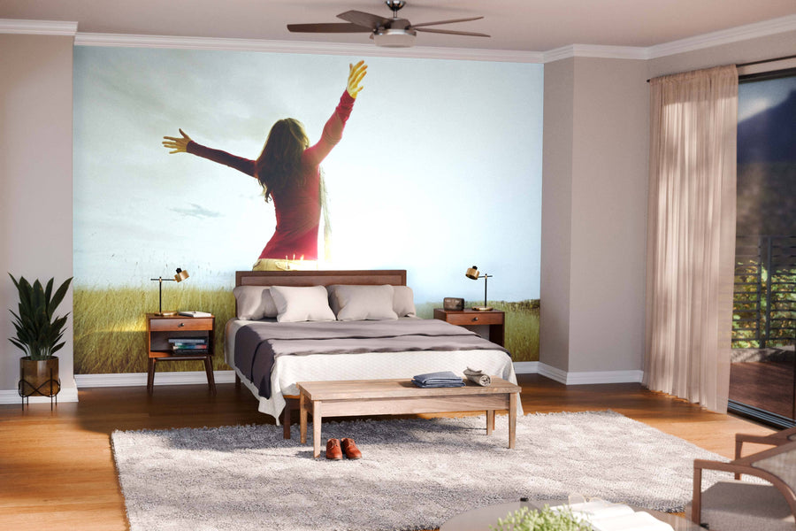 A modern living and dining area with wooden floors, mid-century furniture, pendant lights, and rugs features the Spreading Hands with Joy Wall Mural on a feature wall, separating the kitchen in the background.
