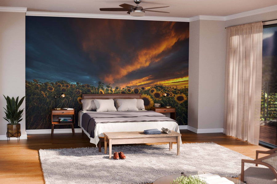 A modern open-plan living and dining room with wooden floors, mid-century furniture, and a large Sunflower Field in Bas-Rhin Wall Mural showing a dramatic sunset. Warm lighting, a rug, and the kitchen area complete this inviting space.