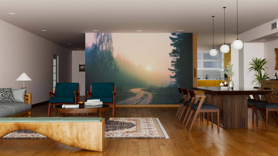 A modern living-dining room features wood floors, green armchairs, a wooden table, pendant lights, and the "Sunrise on a Foggy Forest Road Wall Mural," creating a serene, nature-inspired atmosphere.