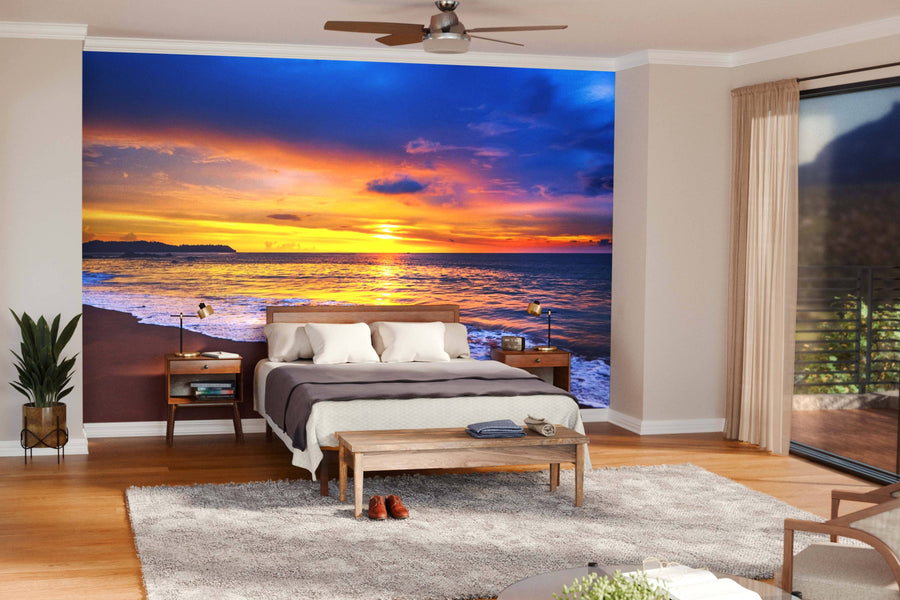 A modern open-concept living and dining area, with wooden floors and mid-century furniture, features the "Sunset Over the Blue Sea Wall Mural," adding vibrant blues, oranges, and yellows of a beach sunset with waves to the space.