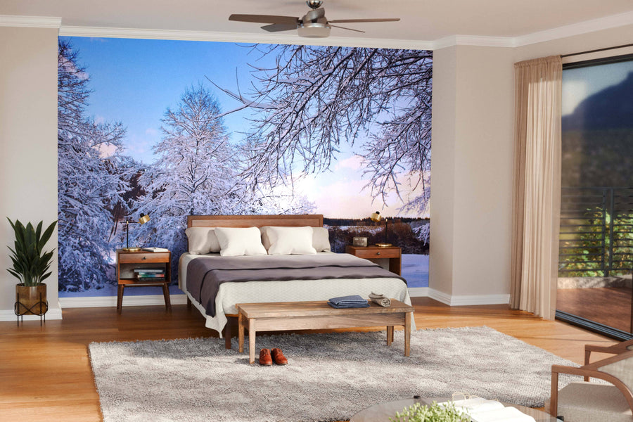 A modern open-plan living and dining room with wooden floors, teal armchairs, and a large dining table is filled with natural light from a wall-sized window and the Trees with Snow in Winter Wall Mural depicting snowy trees and blue sky.