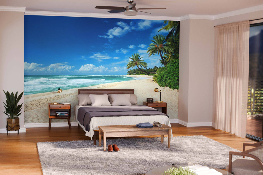 A modern living-dining room features wooden floors, stylish furniture, and the Untouched Sandy Beach Wall Mural with palm trees, blue sky, and ocean waves, adding a vibrant, relaxing touch to the neutral-toned space.