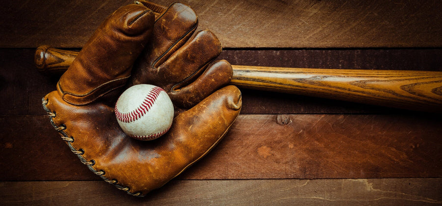 A modern bedroom features a Vintage Baseball Gear Wall Mural with a glove, bat, and ball behind a desk and bed. Sunlight filters through blinds, a soccer ball sits near the bed, and white cabinets are seen on the right.