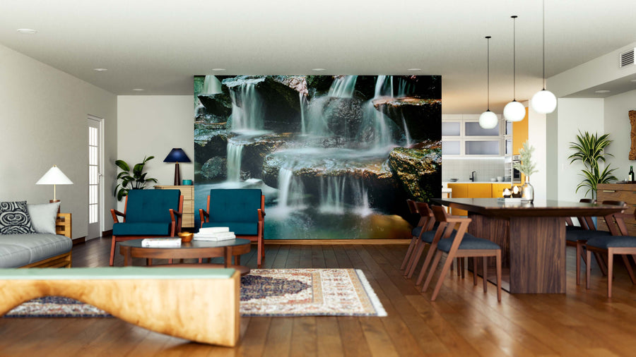 A modern living-dining area features wood floors, blue chairs, a large Water fall Wall Mural on the back wall, pendant lights, a beige sofa, and a wooden dining table. The bright, open space includes a partially visible kitchen.