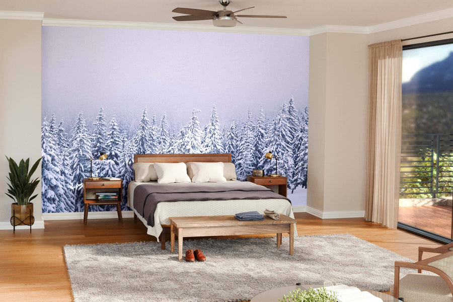 A modern living-dining area features wood floors, teal armchairs, a gray sofa, a wooden dining table, and pendant lighting. The back wall displays the "Winter Trees on Mountain Wall Mural," adding a cozy touch to the minimal space.