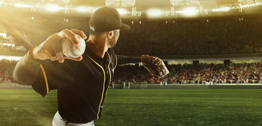 A bedroom features the About to Pitch Wall Mural, showing a baseball pitcher mid-throw in a stadium. The room includes a desk, chair, bed, two sports pictures, a basketball, white cabinets, and sunlight streaming through window blinds.
