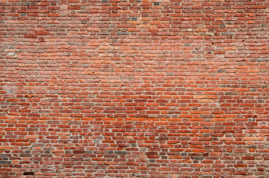 A modern living-dining room showcases the Aged Red Bricks Wall Mural, wooden floors, teal armchairs, a gray sofa, long dining table with chairs, pendant lights, houseplants, rugs, and a glimpse of a yellow kitchen in the background.