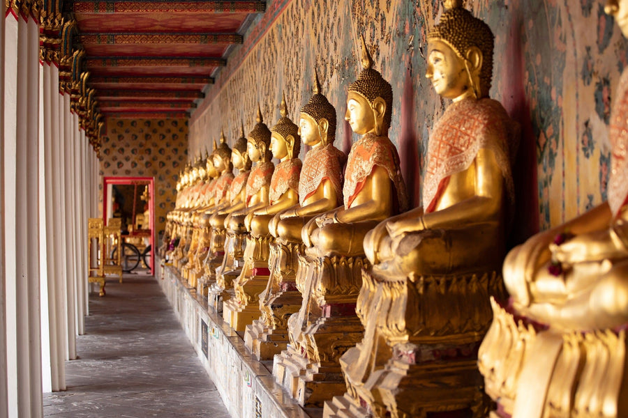 A modern living-dining area with wooden floors, teal chairs, and a rug features the "Buddhas in Wat Pho Temple Wall Mural" along one wall. Spherical pendant lights hang above the table, with kitchen views in the background.