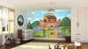 A nursery features the Ark Adventure Wall Mural with animals, a rainbow, and mountains. The room includes a crib, wicker basket, rug, toy rocking horse, light curtains, and sunlight streaming through the window.