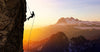 A silhouetted rock climber scales a steep cliff at sunset with glinting safety ropes. The mountain range, featuring a snow-capped peak, is bathed in golden light like the Ascent of Courage Wall Mural. A gradient sky of orange, pink, and blue enhances this dramatic scene.