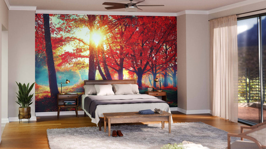 A cozy bedroom with a large bed, wooden furniture, soft gray rug, and an Autumn Fall Nature Scene Wall Mural of sunlit red trees behind the bed; sunlight pours in through sheer curtains on tall windows.