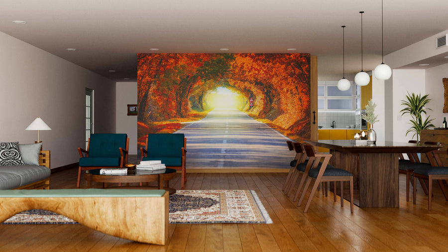 A modern living and dining room features wood floors, teal armchairs, a gray sofa, and the Autumn Fall Road Wall Mural showing a sunlit forest with autumn leaves. A wooden dining table, chairs, and pendant lights complete the space.