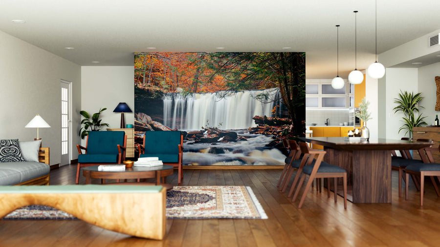 A modern living and dining area showcases wooden furniture, teal chairs, a rug, and the Autumn Waterfalls Wall Mural with autumn foliage, bringing nature indoors. Pendant lights hang above the table and the kitchen appears in the background.