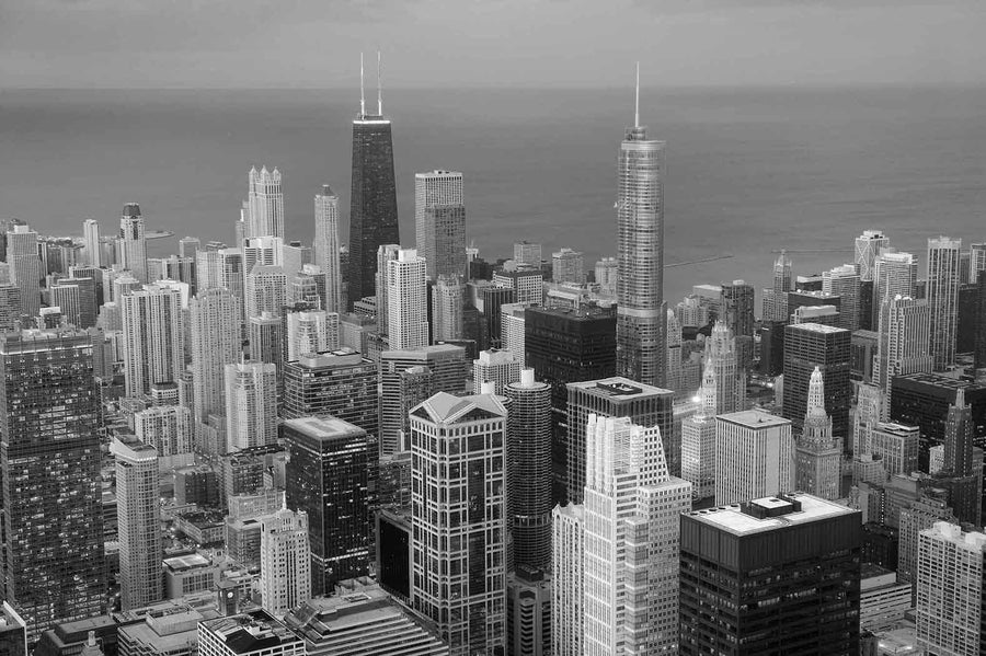 The Chicago Aerial View Hancock Building Wall Mural captures a stunning cityscape at dusk, featuring illuminated skyscrapers and tall buildings against a calm lake. The soft blue evening sky and vibrant city lights create an ideal urban atmosphere for custom printed murals.