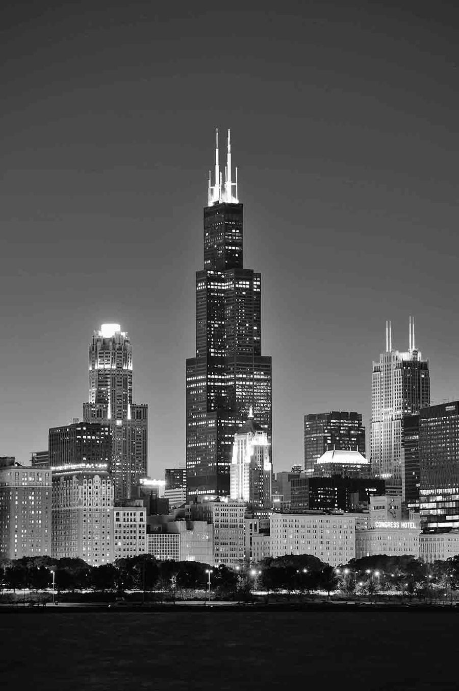 The night skyline displays a tall, lit skyscraper with antennas at its center, surrounded by illuminated buildings under a deep blue gradient sky, mirroring the vibrant urban feel of the Chicago Willis Sears Tower Wall Mural.